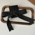 Detail of a dark gray knitted bow hair clip on a branded card in a wooden tray - Dark Gray