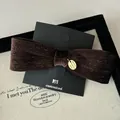 Macro detail of dark brown velvet bow hair clip with silver stripes and gold logo tag - Latte Coffee