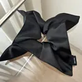Detail of a large black satin scrunchie with handmade label and glossy silk texture - Black