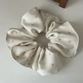 Macro-opname van beige geplooide scrunchie met zilveren glitterstippen en geribbelde textuur - Broken Wit