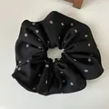 Gros plan détaillé d'un chouchou noir avec des paillettes argentées sur tissu - Noir