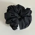 Gros plan du chouchou noir en tissu texturé avec étiquette tissée Hand Made - Noir