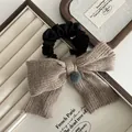 Détail d'un nœud tricoté kaki avec pompon gris sur chouchou noir élégant - Tricot / Khaki