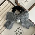 Détail d'un chouchou noeud en peluche grise avec pompon en fourrure et satin doux - Peluche / Gris