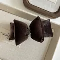 Dettaglio del fermaglio a fiocco in velluto marrone scuro con perle argentate in box - Marrone