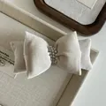Dettaglio ravvicinato del fermaglio a fiocco in velluto crema con perle eleganti - Beige