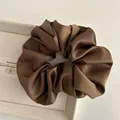 Detailed close-up of dark brown satin scrunchie with soft pleats on a textured tray - Brown