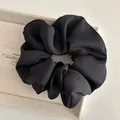 Close-up of black satin oversized scrunchie with elegant pleated silk texture on beige box - Black