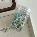 Close-up of colorful braided elastic hair ties stored in a transparent plastic jar - Macaron Series