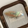 Macro detail of marbled acetate hair clip with golden Flower Handmade text on fabric - Iridescent Orange