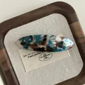Macro detail of oval acetate hair clip with marble texture and gold lettering - Contrast Blue Coffee