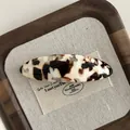 Detail view of oval tortoiseshell acetate hair clip on a natural linen background - Contrast Milk Coffee