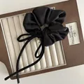 Dettaglio di scrunchie in raso nero con fiocco, finitura lucida e ciondolo di perla - Nero