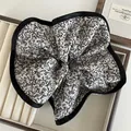 Detail of oversized floral scrunchie with black satin piping edge in a wooden display box - Beige