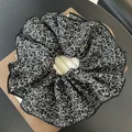 Detalle de coletero grande negro con flores blancas en soporte de cartón marrón - Negro