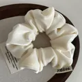 Close-up of a plush cream velvet scrunchie featuring a brand label in a wooden tray - Off White