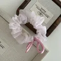 Detail of light pink silk satin scrunchie with sheer mesh ruffles and elegant ribbon bow - Pink
