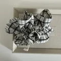 Detail eines karierten Haargummis mit Herkunftsetikett in einer grauen Geschenkbox - Schwarzes Gitter