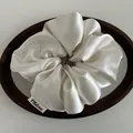 Close-up of white satin scrunchie with FMdrea brand label on a wooden tray - Off White