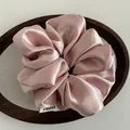 Close-up of a pink satin scrunchie with white brand tag on a wooden tray - Pink