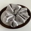 Close-up of a silver satin scrunchie with high glossy texture and a fabric label detail - Silver Gray