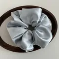 Detail of light blue satin oversized scrunchie with silky texture and woven label - Blue