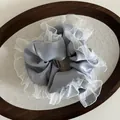 Detail of grey satin scrunchie featuring white pleated organza edges and brand label - Blue