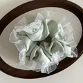 Detail of light green satin scrunchie with white organza ruffled edges on wooden tray - Green