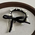 Detalle de elegante lazo negro para el cabello con perlas blancas y colgante metálico - Cinta de Satén Negro Perla