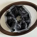 Detail eines eleganten schwarzen Metallic-Haargummis in einem Holz-Display-Tablett - Schwarz