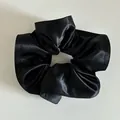 Dettaglio di un elastico per capelli in raso nero con texture a pieghe e finitura lucida - Nero