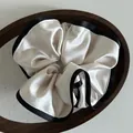 Nahaufnahme von cremefarbenem Satin-Haargummi mit Jacquard-Muster und schwarzem Bandrand - Cremeweiß