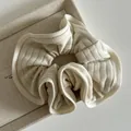 Close-up of cream knit scrunchie texture with elastic ribbed fabric and soft ruffles - Off-white