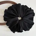 Vue détaillée d'un grand chouchou noir en tissu plissé avec des bords ondulés élégants - Noir