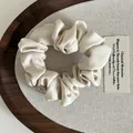 Detail van een crème beige satijnen scrunchie met zachte zijden textuur in houten dienblad - Off-wit
