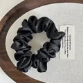 Detailopname van een zwarte satijnen scrunchie met zijdeglans op geweven achtergrond - Zwart