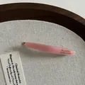 Détail macro d'une barrette en acétate rose avec lettrage doré sur support en toile - Rose
