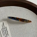 Détail macro d'une barrette en acétate avec motif écaille bleue et logo doré élégant - Bleu Marron