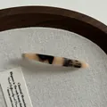 Détail d'une barrette en acétate écaille de tortue avec inscription dorée sur fond lin - Écaille Claire