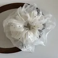 Chouchou élégant en organza blanc cassé à pois noirs sur un plateau en textile gris - Blanc