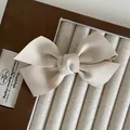 Eleganter beigefarbener Schleifen-Haarclip aus Satin auf einer Samt-Schmuckpräsentation - Beige