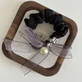 Detail of black scrunchie with purple organza bow and golden bead on rustic linen - Grey Brown