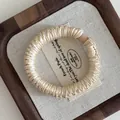 Close-up of a beige satin pleated scrunchie on a wooden tray with elegant textures - Champagne