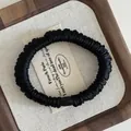 Detail of black pleated satin hair tie with smooth oval bead on elegant canvas texture - Black