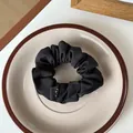 Detail of a black fabric scrunchie with minimal logo tag on a ceramic plate - Black