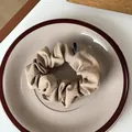 Detailed view of a khaki pleated scrunchie made of soft fabric on a ceramic tray - Light Coffee