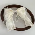 Detail of cream satin and organza bow hair clip with faux pearl trim and elegant long streamers - Beige