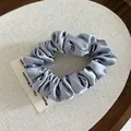 Macro detail of silver satin scrunchie with pearl sheen on a wooden tray setting - Blue