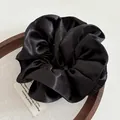 Detailed view of premium black satin scrunchie with elegant pleated silk texture on a wooden tray - Black