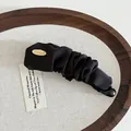 Detailansicht der schwarzen Satin-Bananenspange mit goldener Metallscheibe auf Holztablett - Schwarz